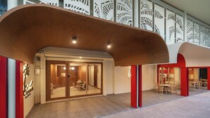 Een modern gebouw met een gebogen houten dakoverhang, glazen deuren die leiden naar een binnenruimte met zitplaatsen, en een wand met een decoratief patroon.