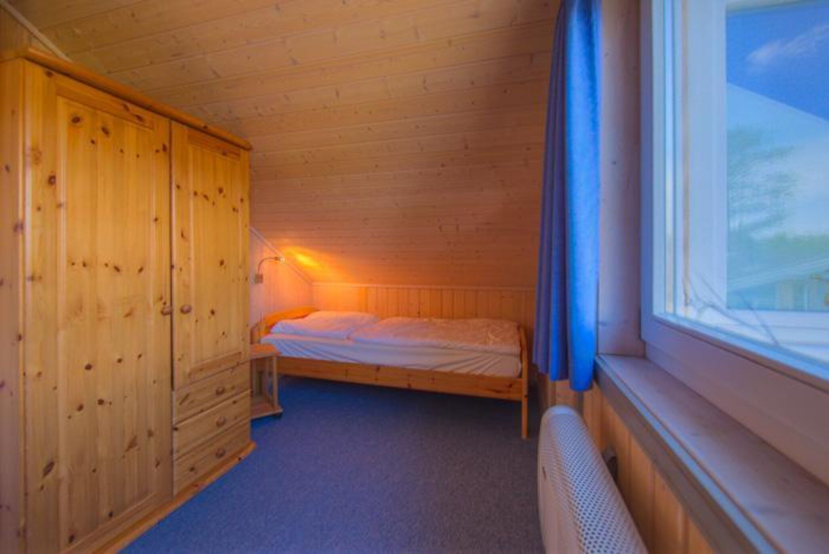 A small, cozy room with a single bed, a wooden wardrobe, and a window with curtains.