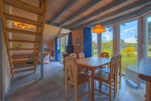 A wooden interior with a dining table and chairs, a TV, and a view of the outdoors.