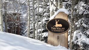 A sign for "The Villas at Snowmass Club" with a deer logo, surrounded by snow-covered trees. - Villas at Snowmass Club - 1207 (Snowmass Village)