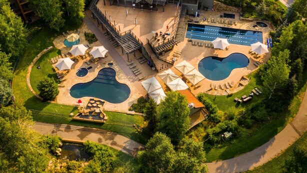 An aerial view of a resort with multiple swimming pools, outdoor seating areas, and a large building with a distinctive roof. - Villas at Snowmass Club - 1207 (Snowmass Village)