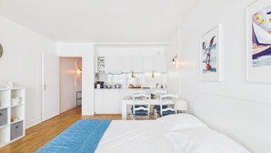 A bedroom with a bed, a blue rug, a kitchenette, and a dining area. - -BLUE- STUDIO AVEC VUE MER ET PARKING (Concarneau)