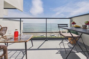 A balcony with a glass table, wicker chairs, a red drink, and a view of the sea.