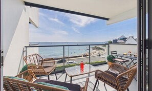 A balcony with wicker furniture, a glass table, and a view of the beach and ocean.