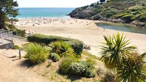 A beach with people, a clear sky, and a rocky hillside. - -BLUE- STUDIO AVEC VUE MER ET PARKING (Concarneau)