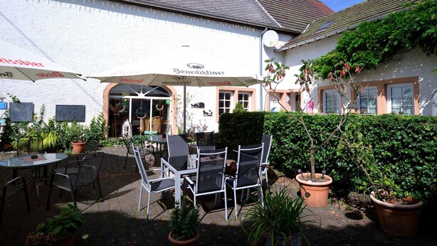 An outdoor seating area with tables and chairs, a white building with a sign reading "Benediktiner," and potted plants. - Apartment in Meisberg With In-house Catering (Meisburg)