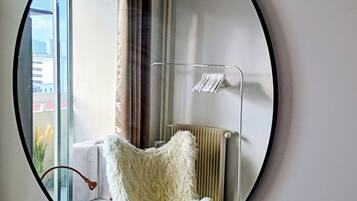 Een ronde spiegel die een kamer weerspiegelt met een zachte fauteuil, een radiator en een raam met gordijnen.