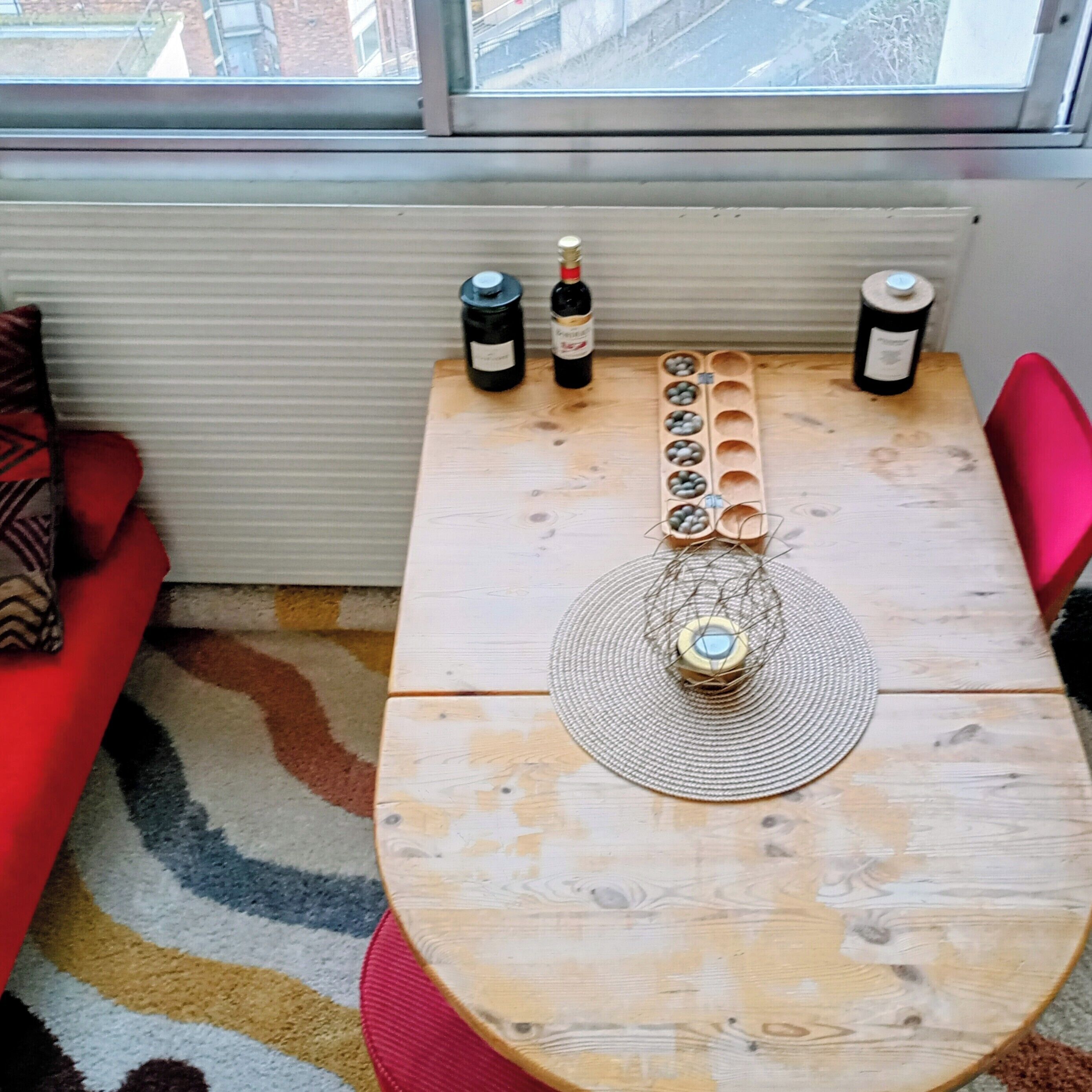 Een houten tafel met een geweven tafelmat, twee flessen wijn en een decoratief middelpunt.