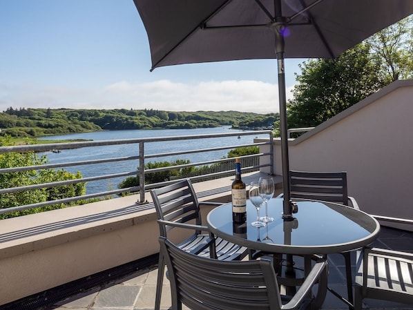A balcony with a table, chairs, and a bottle of wine.