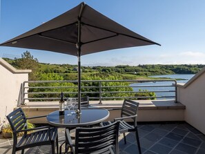A terrace with a table and chairs, a table umbrella, and a view of a lake and greenery.