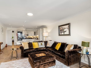 A modern living room with a dark brown sofa set, a coffee table, and a dining area visible in the background. - 4 Harbour Heights Panoramic Bay Views (Clifden)