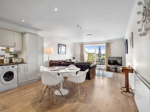 A modern kitchen with white cabinets, a washing machine, and a dining area with a white table and chairs. - 4 Harbour Heights Panoramic Bay Views (Clifden)