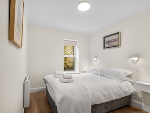 A bedroom with a bed, two bedside tables, a window, and a radiator.