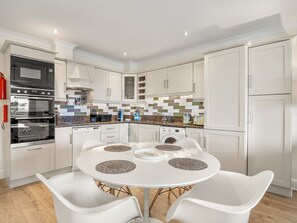 A modern kitchen with white cabinetry, a built-in oven, and a round dining table with chairs.