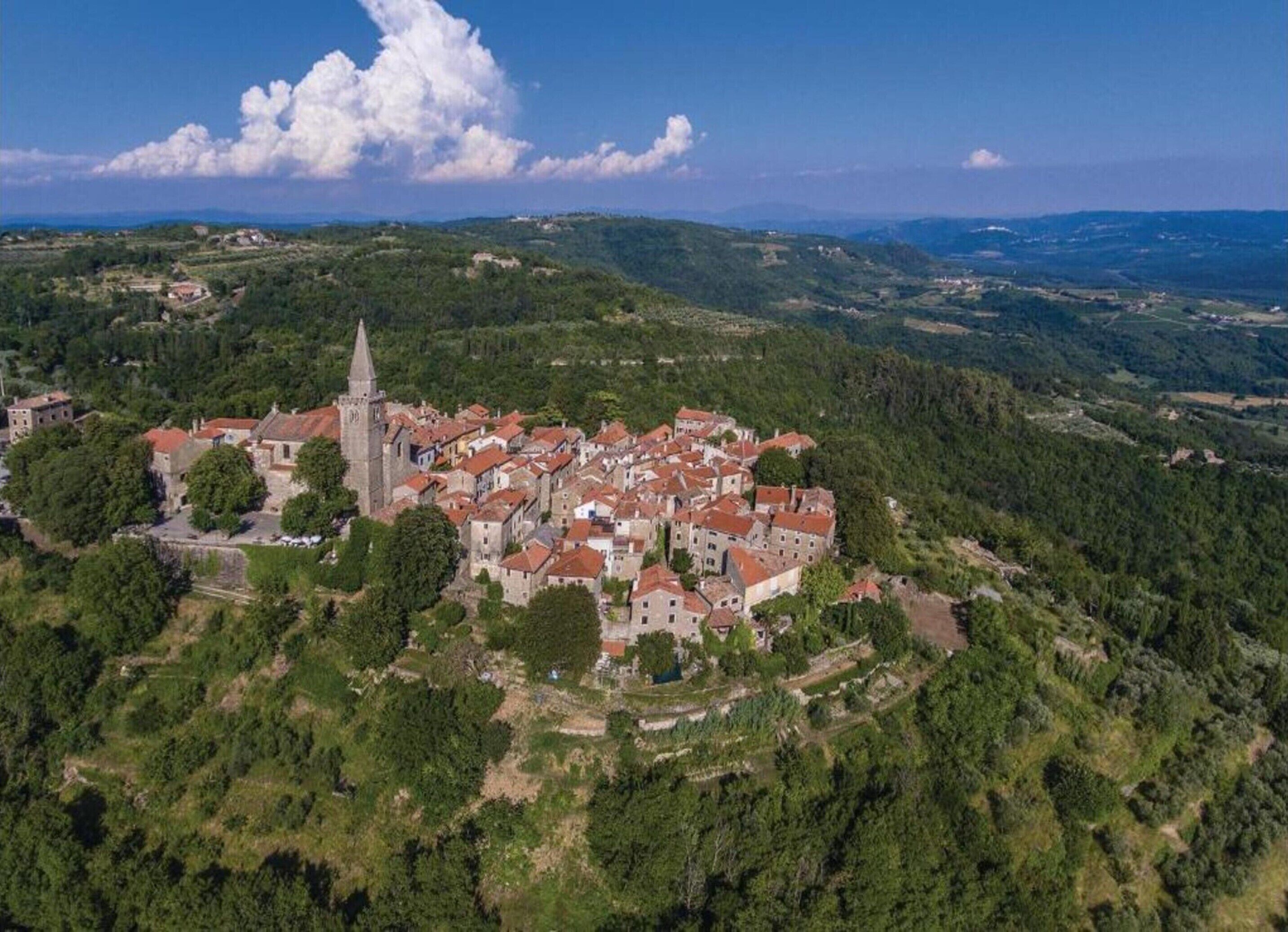 An aerial view of a historic town with a prominent church tower, surrounded by lush greenery and rolling hills.