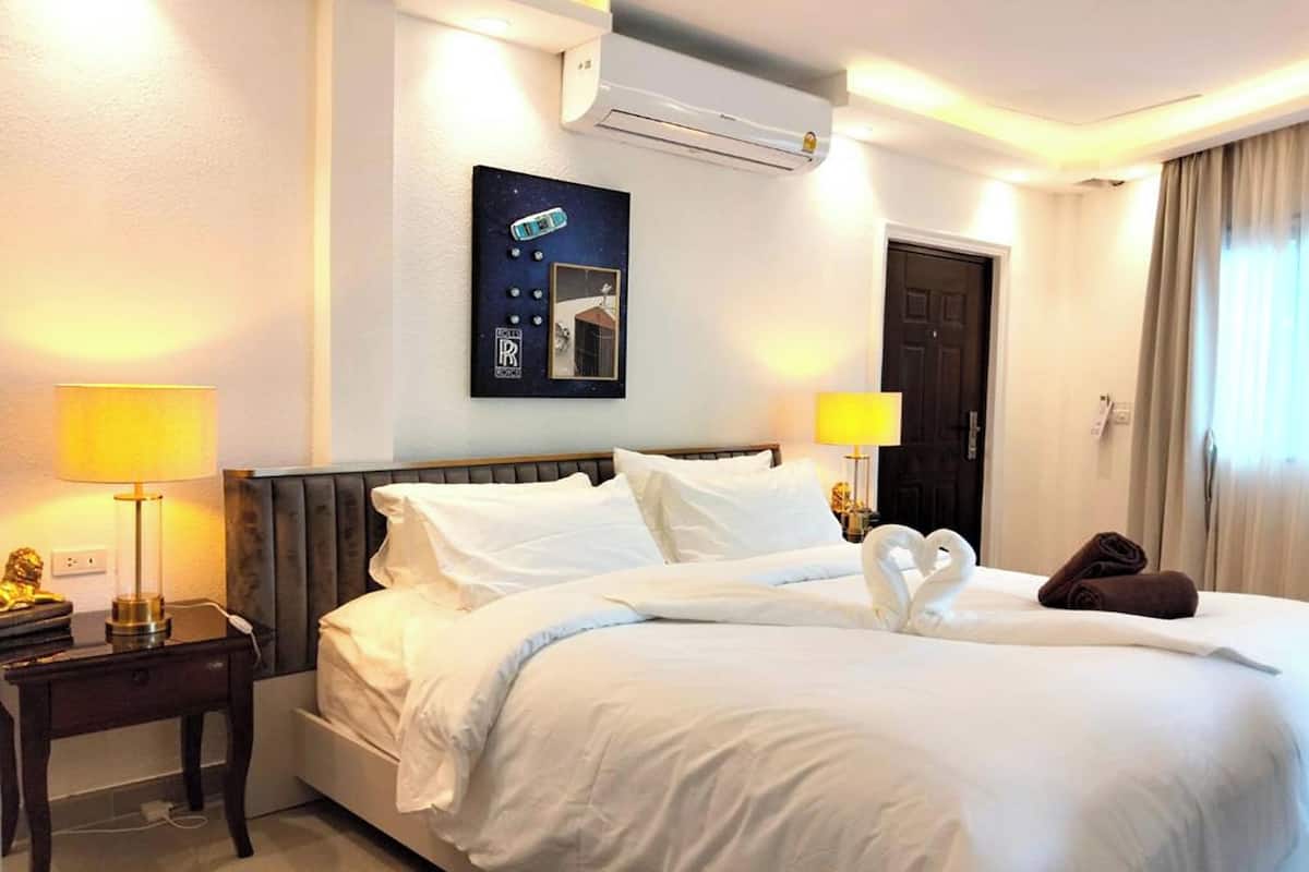Ein Hotelzimmer mit einem Bett, zwei Nachttischlampen, einer Wandklimaanlage, einem gerahmten Bild und einer Tür.