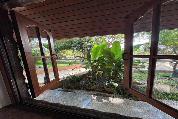 Une porte en bois ouverte donne sur un jardin agrémenté de plantes en pot et d’un chemin de pierres.