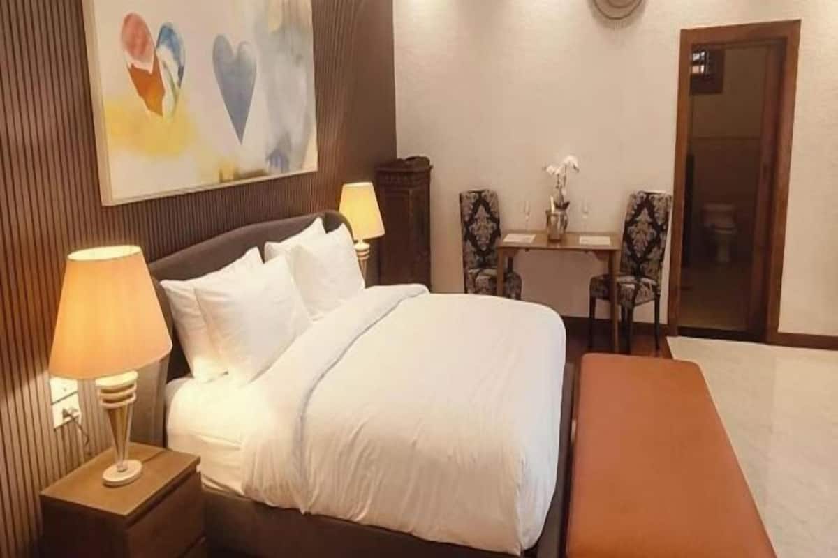 Ein Hotelzimmer mit Bett, Nachttischlampen, einem Schreibtisch mit Stuhl und einem Gemälde an der Wand.
