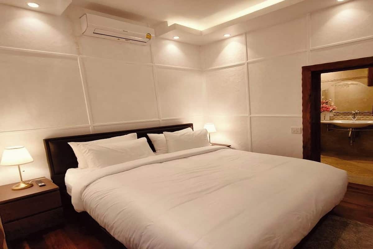 Ein Hotelzimmer mit einem großen Bett, Nachttischlampen, einer Klimaanlage und einem durch eine offene Tür einsehbaren Badezimmer.