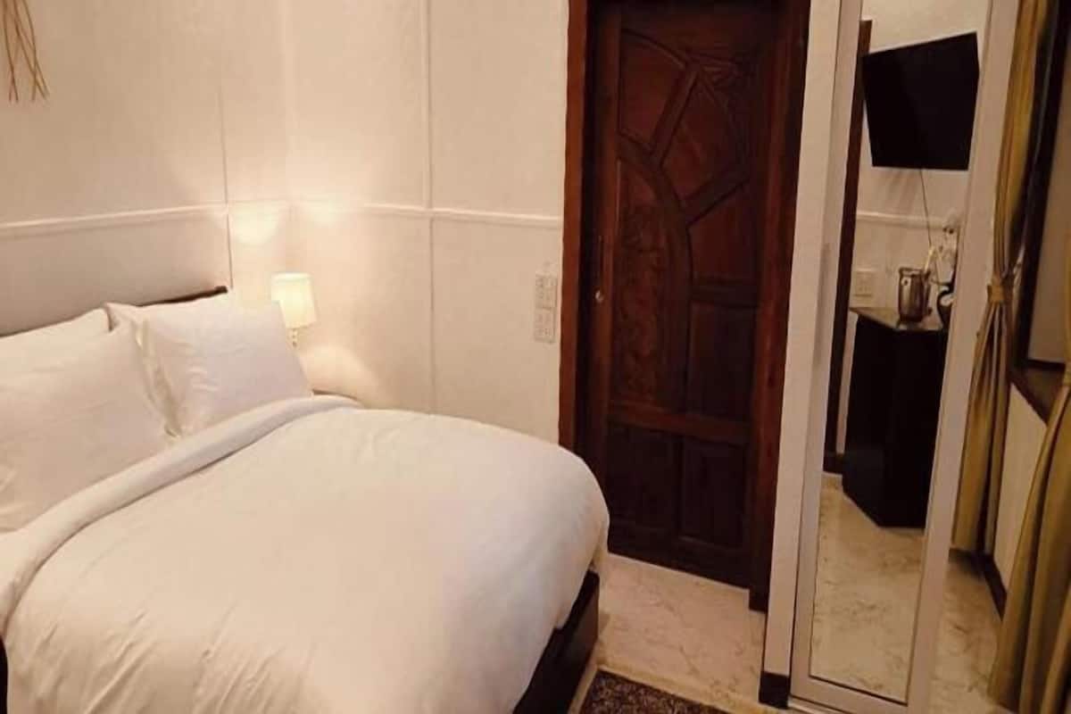 Ein Hotelzimmer mit einem Bett, einer Holztür, einem Spiegel und einer Lampe.