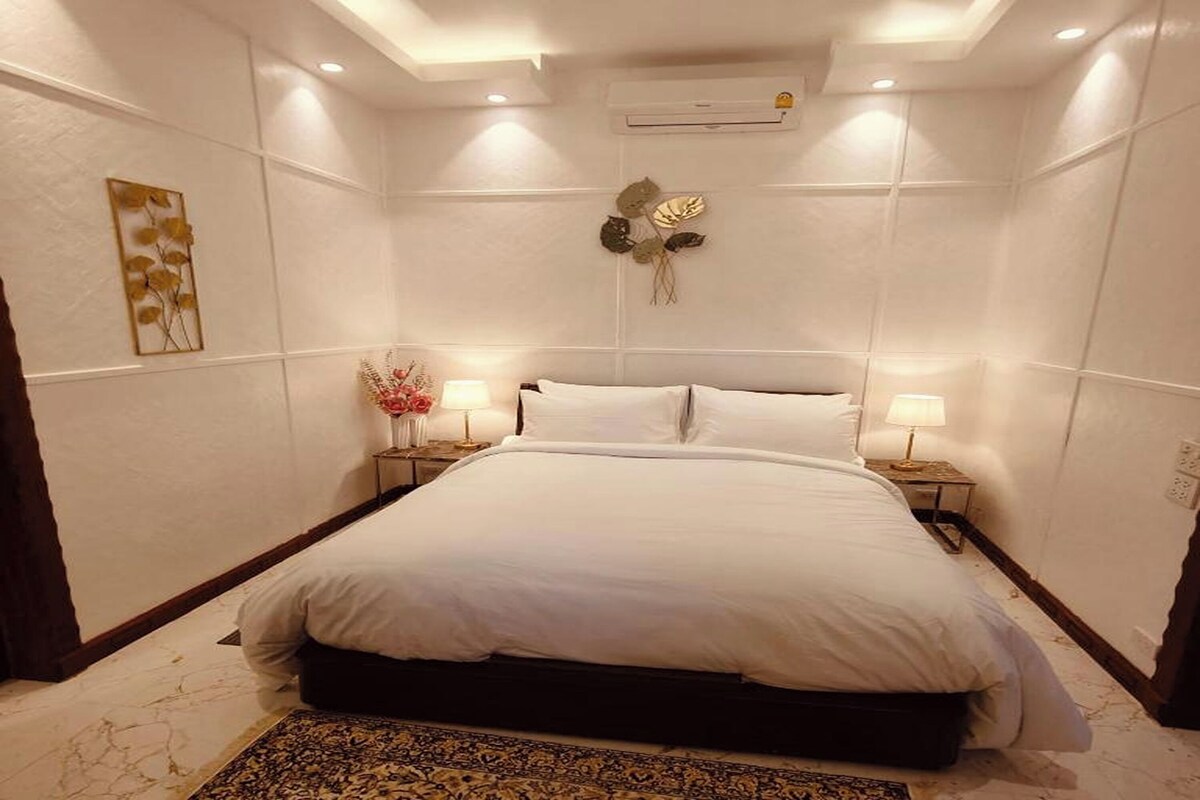 A hotel room with a large bed, two bedside tables, a wall-mounted air conditioner, and a decorative wall piece.
