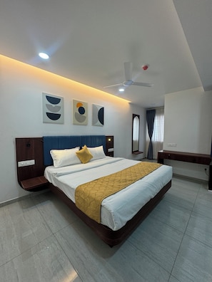 A modern hotel room with a large bed, a bedside table, a desk, and a ceiling fan. - Hotel Grand Kakatiya (Hanmakonda)