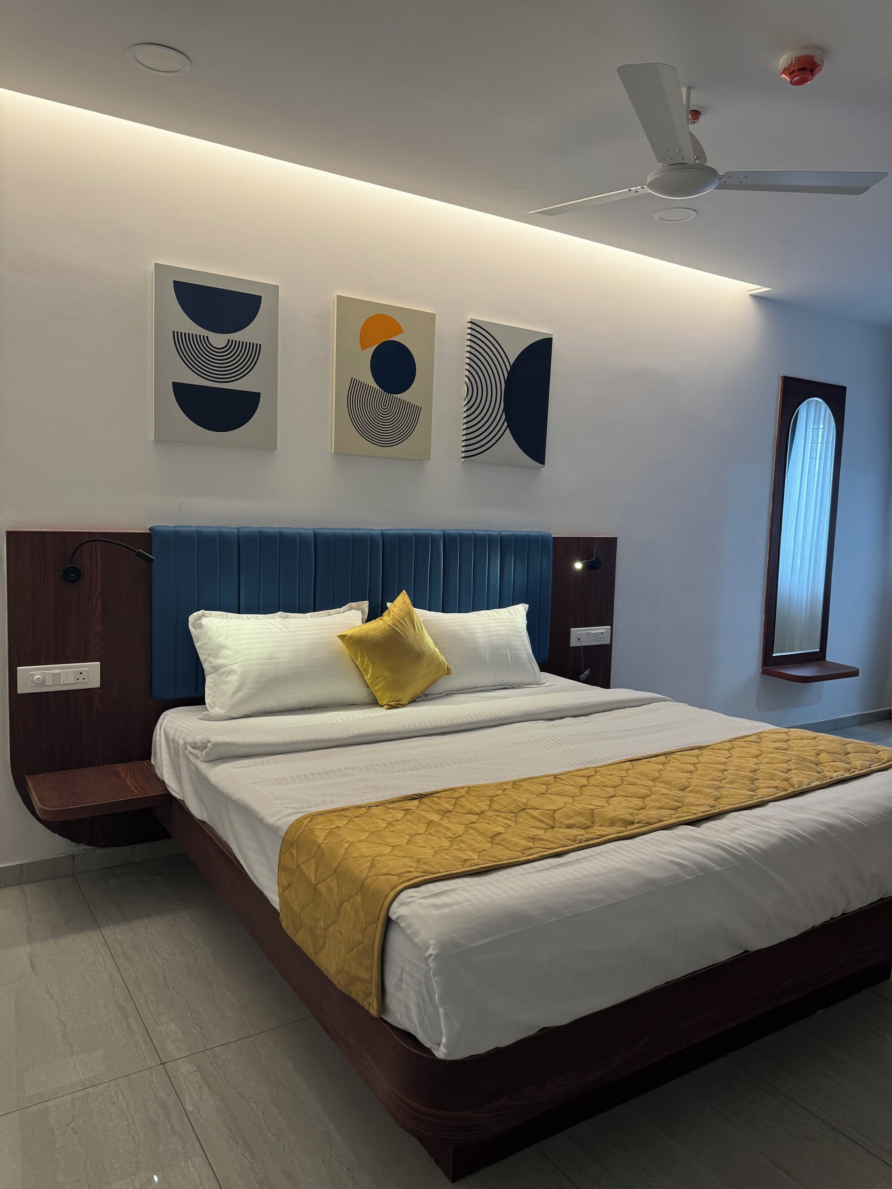 Una habitación de hotel moderna con una cama grande, cabecera azul y una obra de arte en la pared.