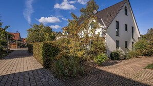 Un immeuble résidentiel avec un toit en tuiles, entouré d’un jardin et bordé d’un chemin pavé.