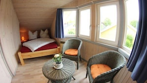 A cozy room with a bed, two wicker chairs, a small table with a flower, and large windows with curtains. - Exklusives Skandinavisches Ferienhaus (Mirow)