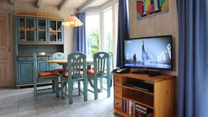 A cozy room with a wooden ceiling, a dining table with chairs, a television, and a bookshelf. - Exklusives Skandinavisches Ferienhaus (Mirow)