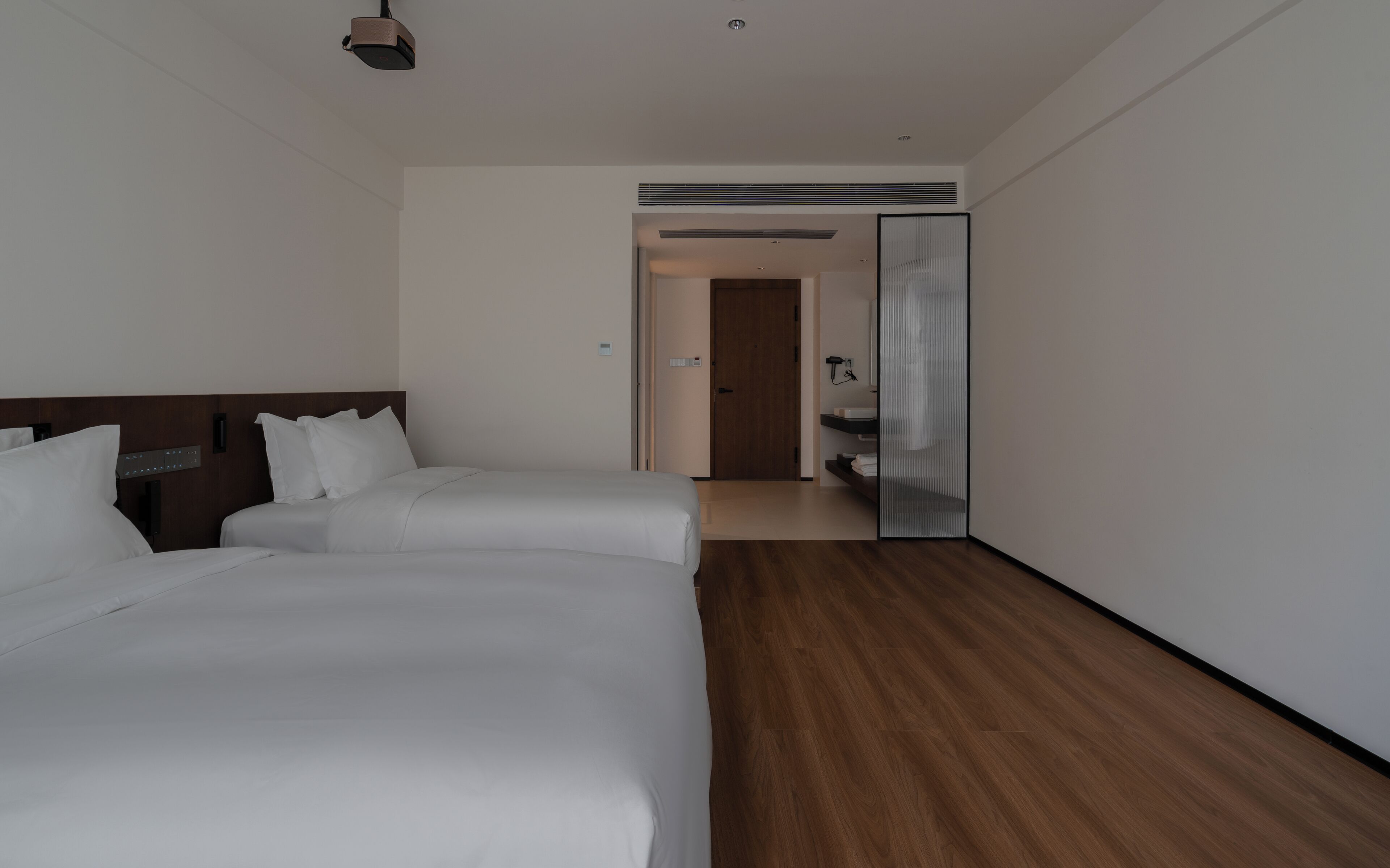 Habitación de hotel con dos camas, suelo de madera, un espejo grande y una puerta que da al baño.