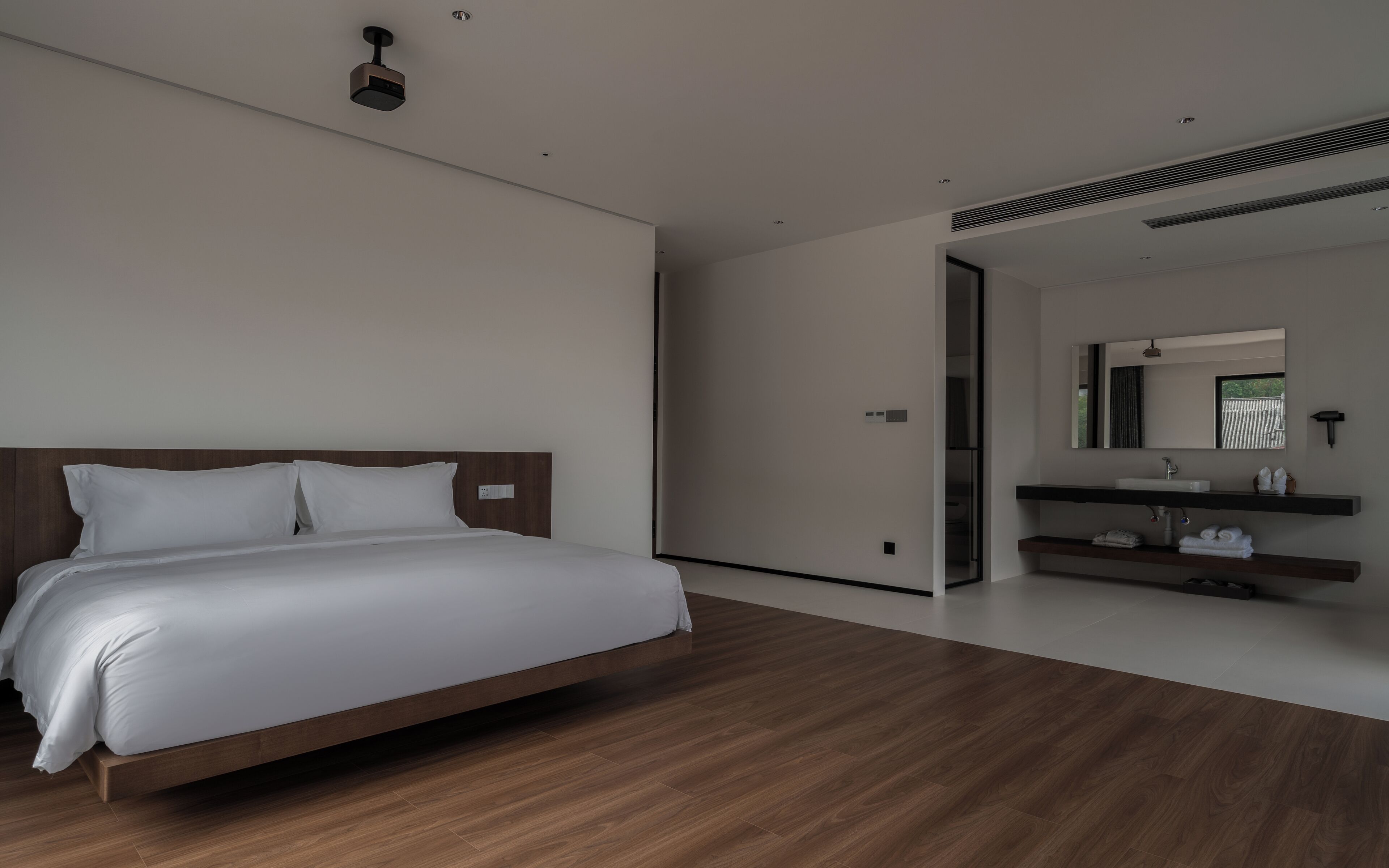 Una habitación de hotel moderna con una cama de madera, un baño con espejo y lavamanos, y piso de madera.