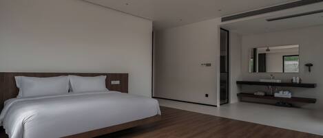 Una habitación de hotel moderna con una cama de madera, un baño con espejo y lavamanos, y piso de madera.