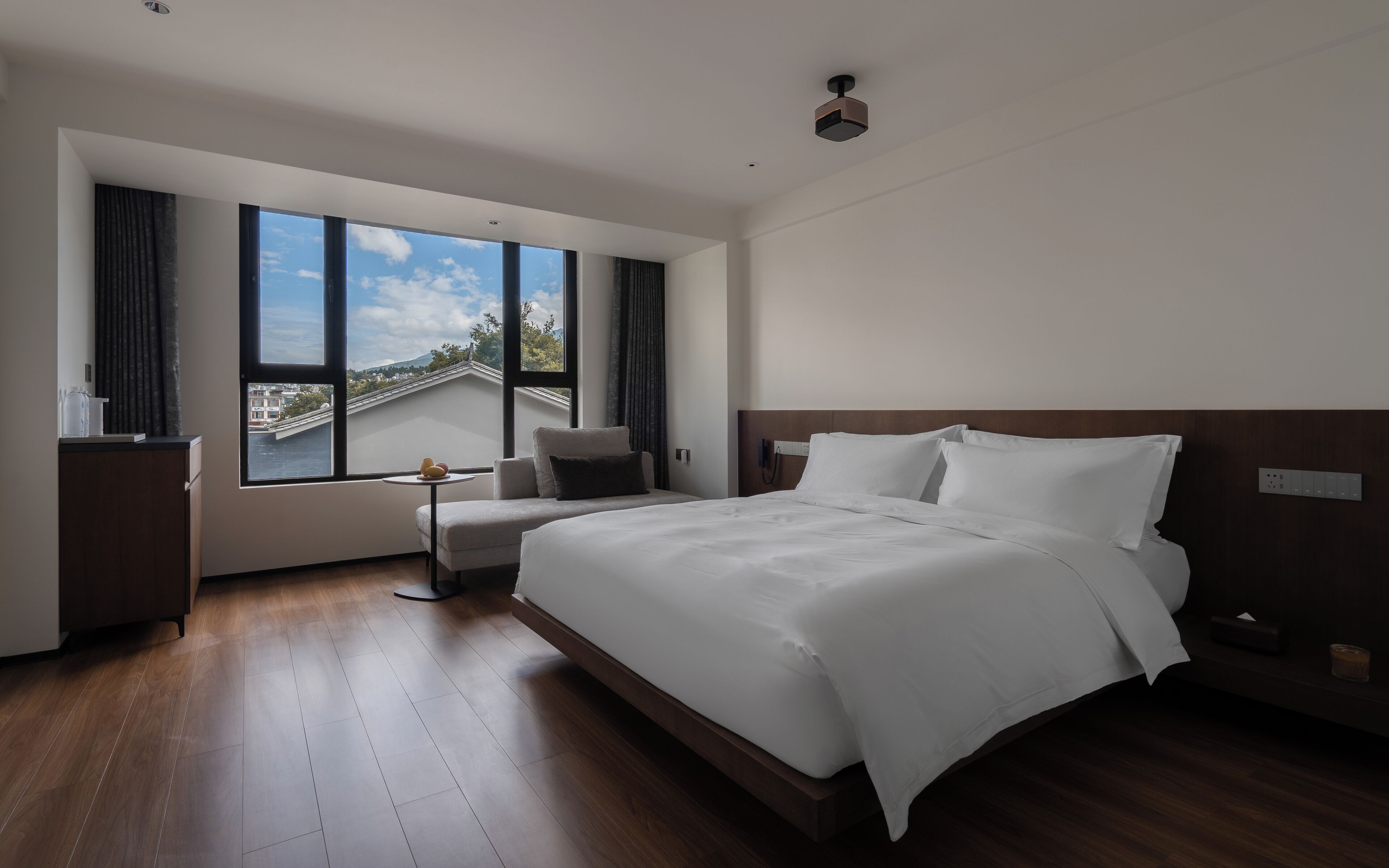 Une chambre d’hôtel moderne dotée d’un grand lit, d’un petit coin salon, d’une vue sur la ville et d’un plancher en bois.