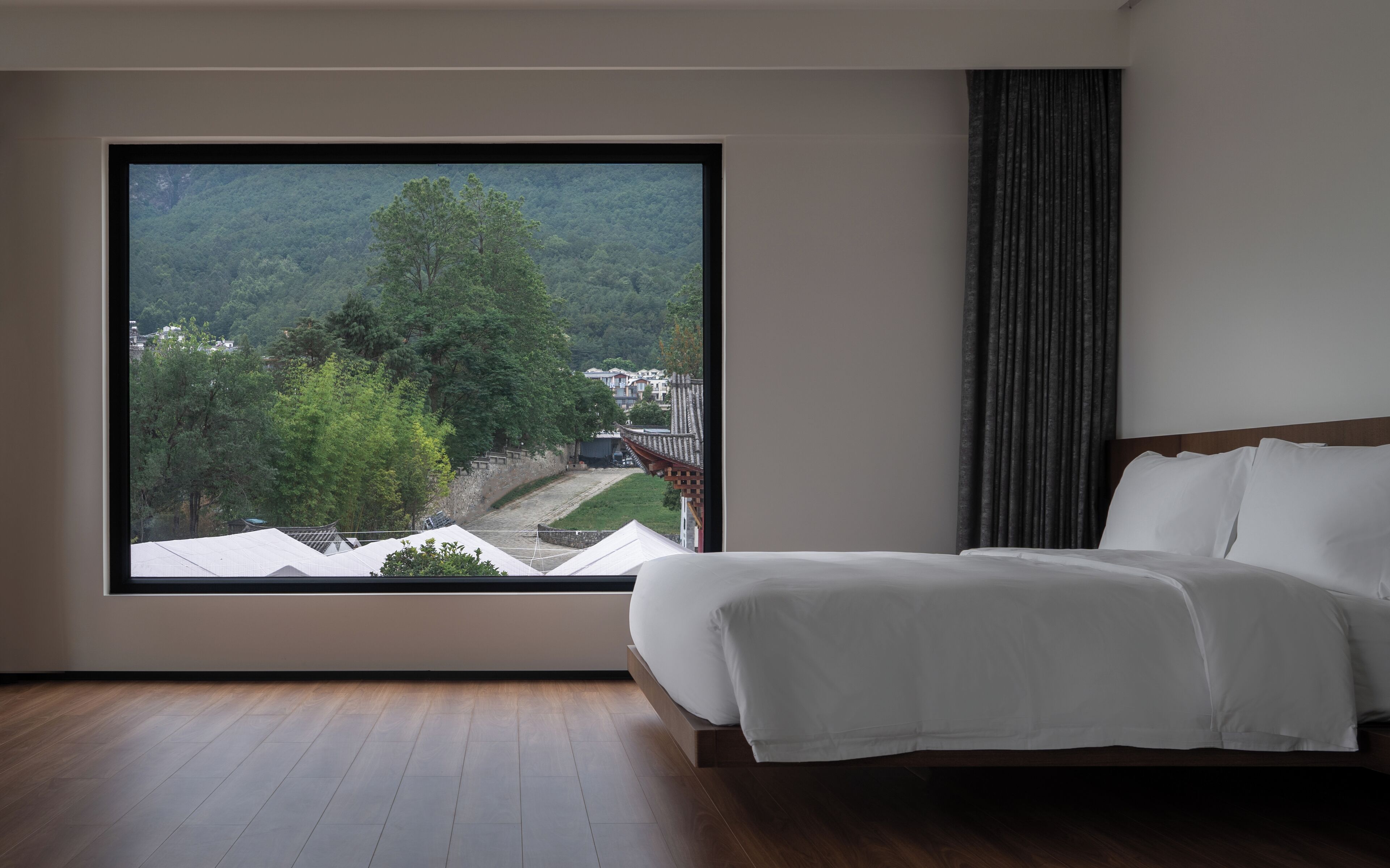 A bedroom with a large window, a bed, and a view of a forested area.