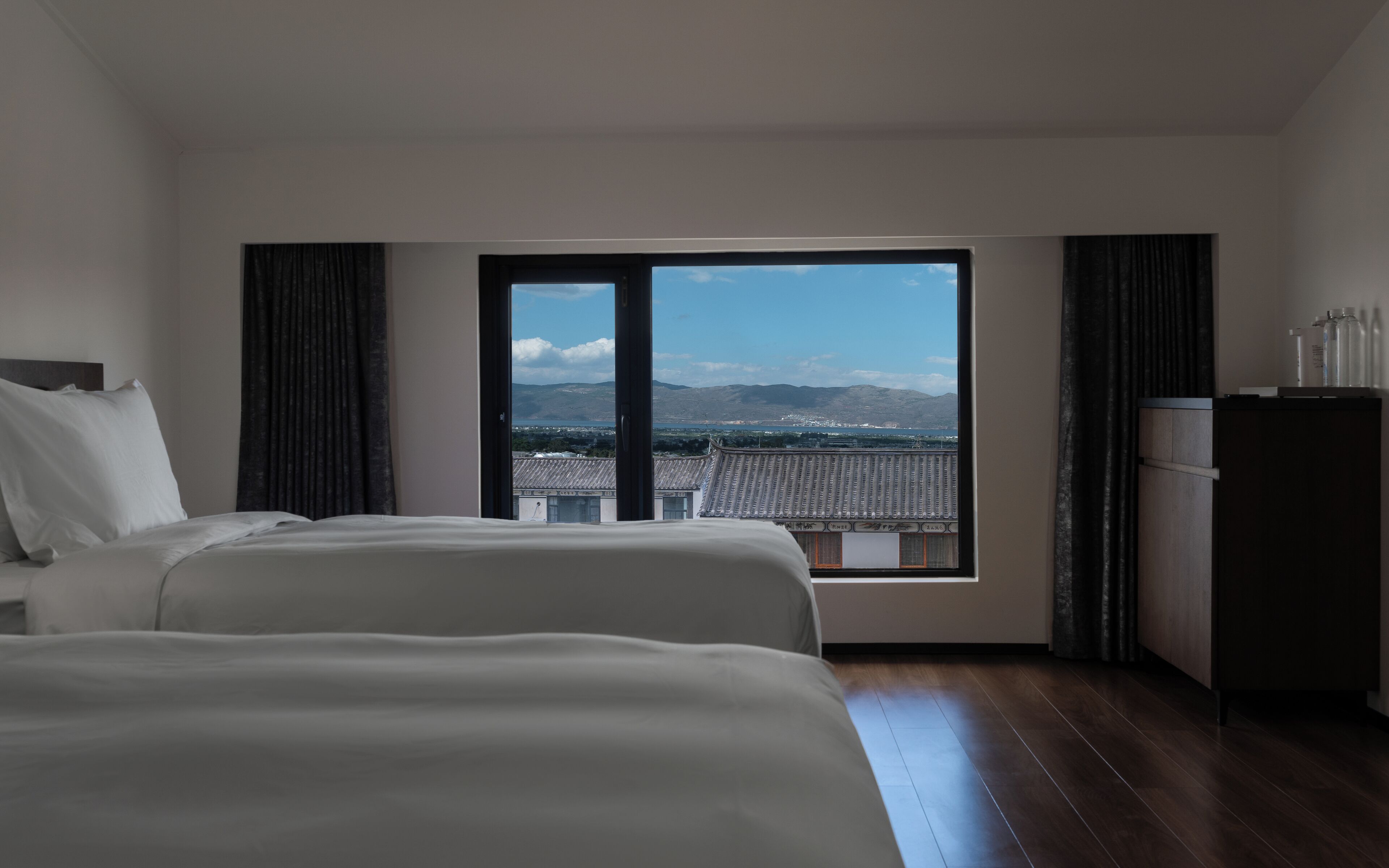 A hotel room with a large window offering a view of a mountainous landscape.