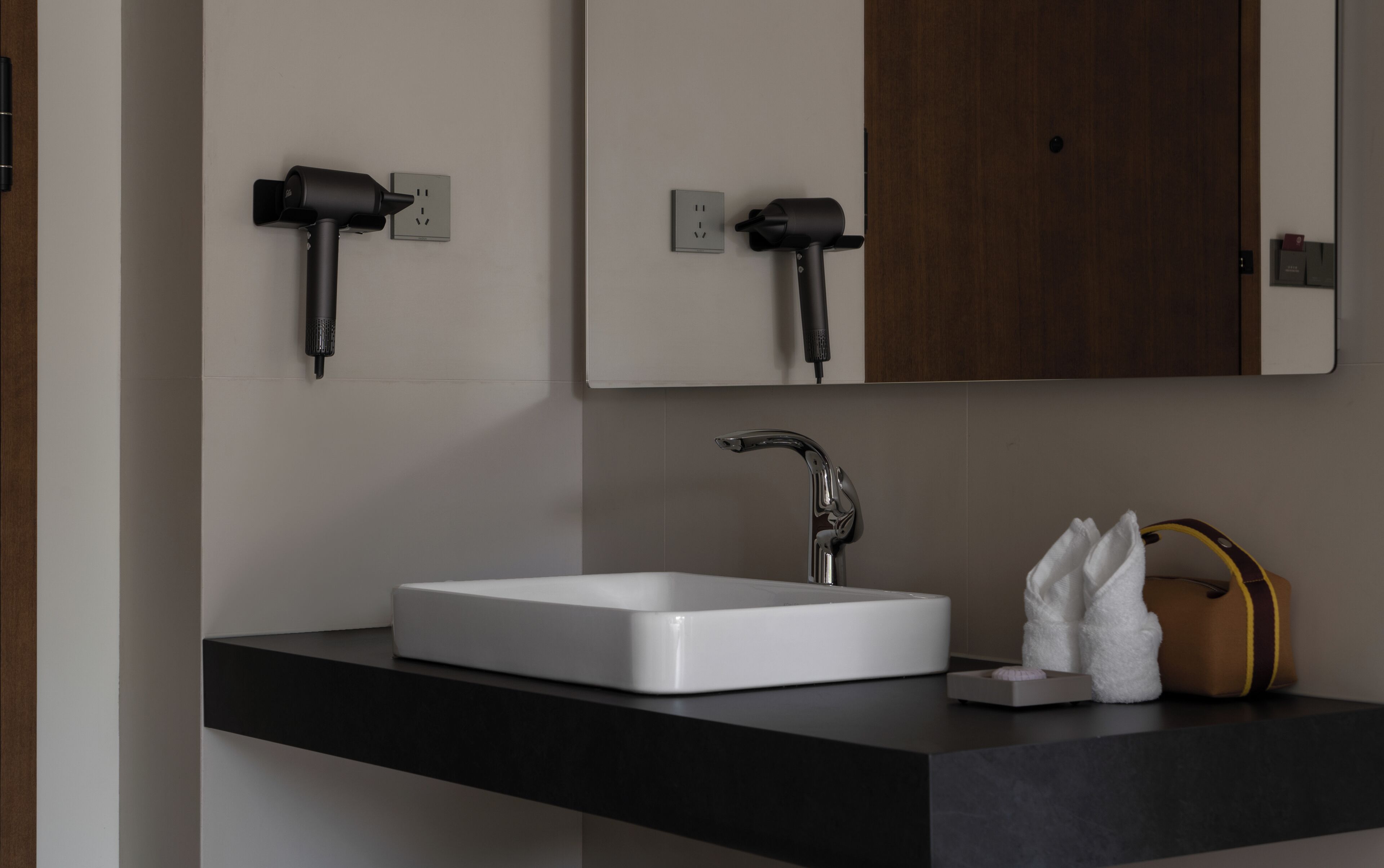 A modern bathroom with a white sink, black countertop, and a wooden door.