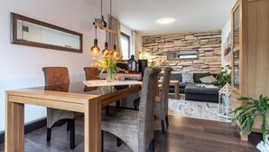 A modern living room with a stone wall, a wooden dining table, and a sofa. - Moderne und Komfortable Ferienwohnung in Busum (Büsum)