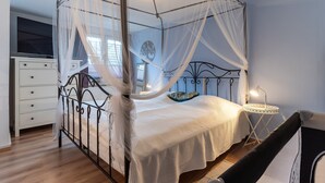 A four-poster canopy bed with a white bedspread, a bedside table with a lamp, and a small round table with a lamp. - Moderne und Komfortable Ferienwohnung in Busum (Büsum)