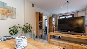 A modern living room with a wooden TV stand, a flat-screen TV, and a dining area with a wooden table and chairs. - Moderne und Komfortable Ferienwohnung in Busum (Büsum)