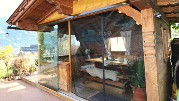 A wooden cabin with a glass enclosure, a wooden deck, and a mountain view. - Apartment in Fugen Near ski Resort (Fuegen)