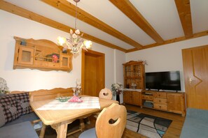 Un coin repas avec une table en bois, des chaises, un lustre et un téléviseur en arrière-plan.