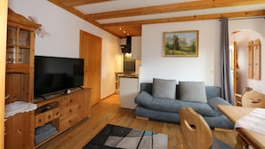 A cozy living room with a wooden cabinet, a flat-screen TV, a blue sofa, and a dining table. - Apartment in Fugen Near ski Resort (Fuegen)