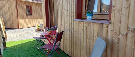 A wooden cabin with a patio area featuring artificial grass, a table with chairs, and a lounge chair.