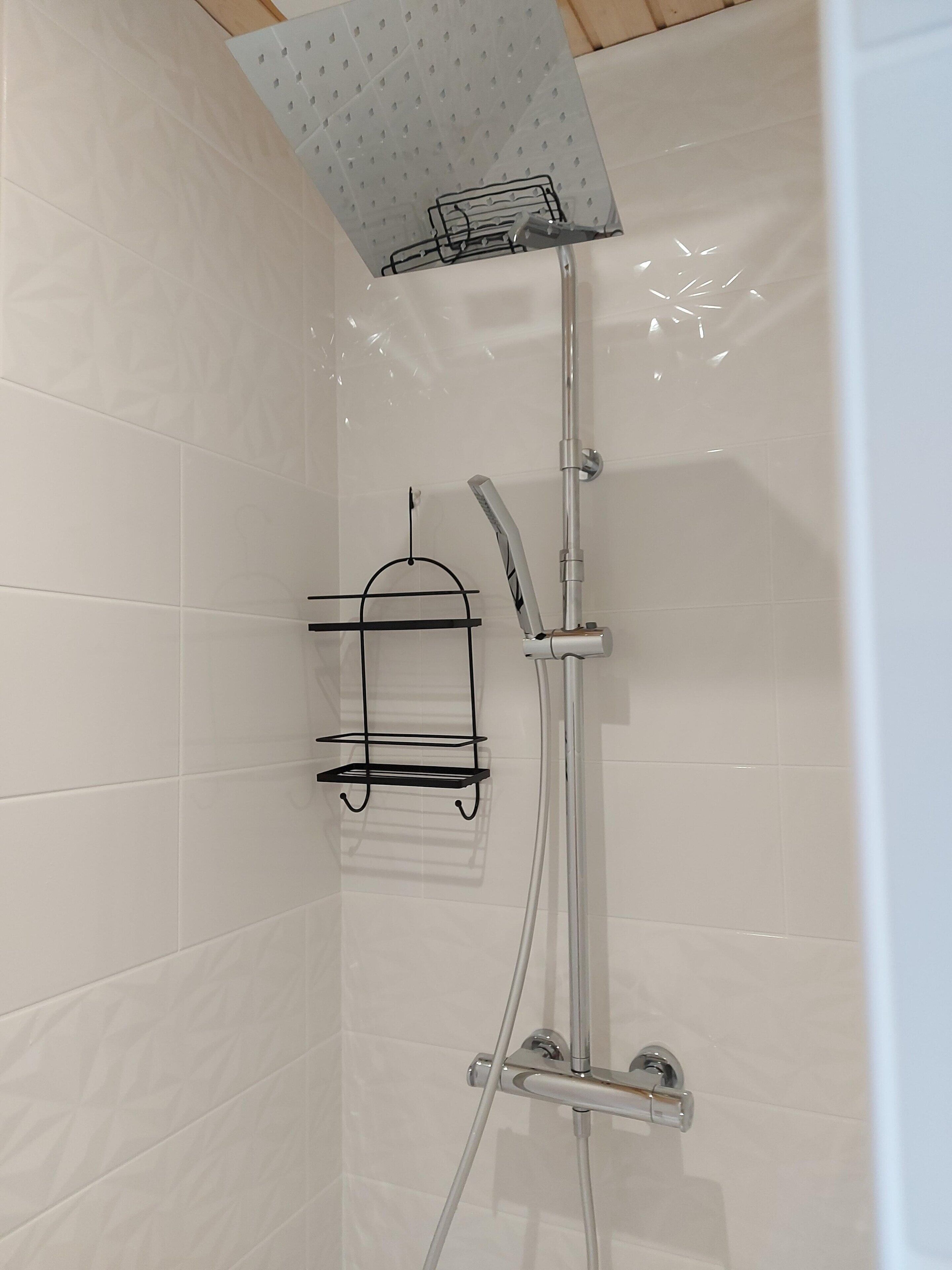 Een douche met een handdouche, een wandmengkraan en een plank voor toiletartikelen.