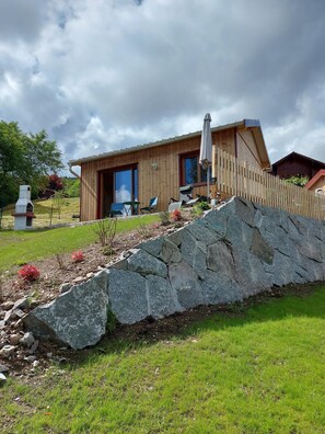 A wooden cabin with a stone retaining wall, outdoor seating, and a chimney. - 2 Chalets for 4 People (Saint-Maurice-sur-Moselle)