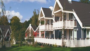 Une rangée de maisons traditionnelles de style scandinave, avec leurs toits pentus et leurs façades blanches, se dressent sur un fond de verdure et sous un ciel dégagé.