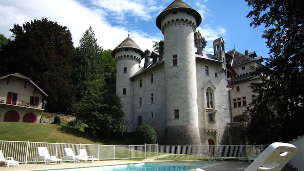 Un château doté d’une piscine, de chaises longues blanches et d’une clôture blanche.