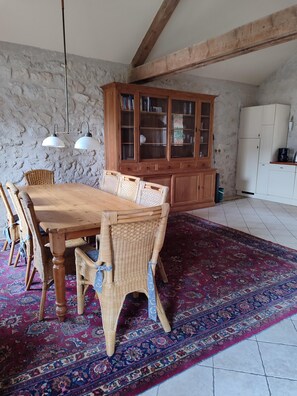 A dining area with a wooden table and wicker chairs, a patterned rug, and a wooden cabinet with glass doors.