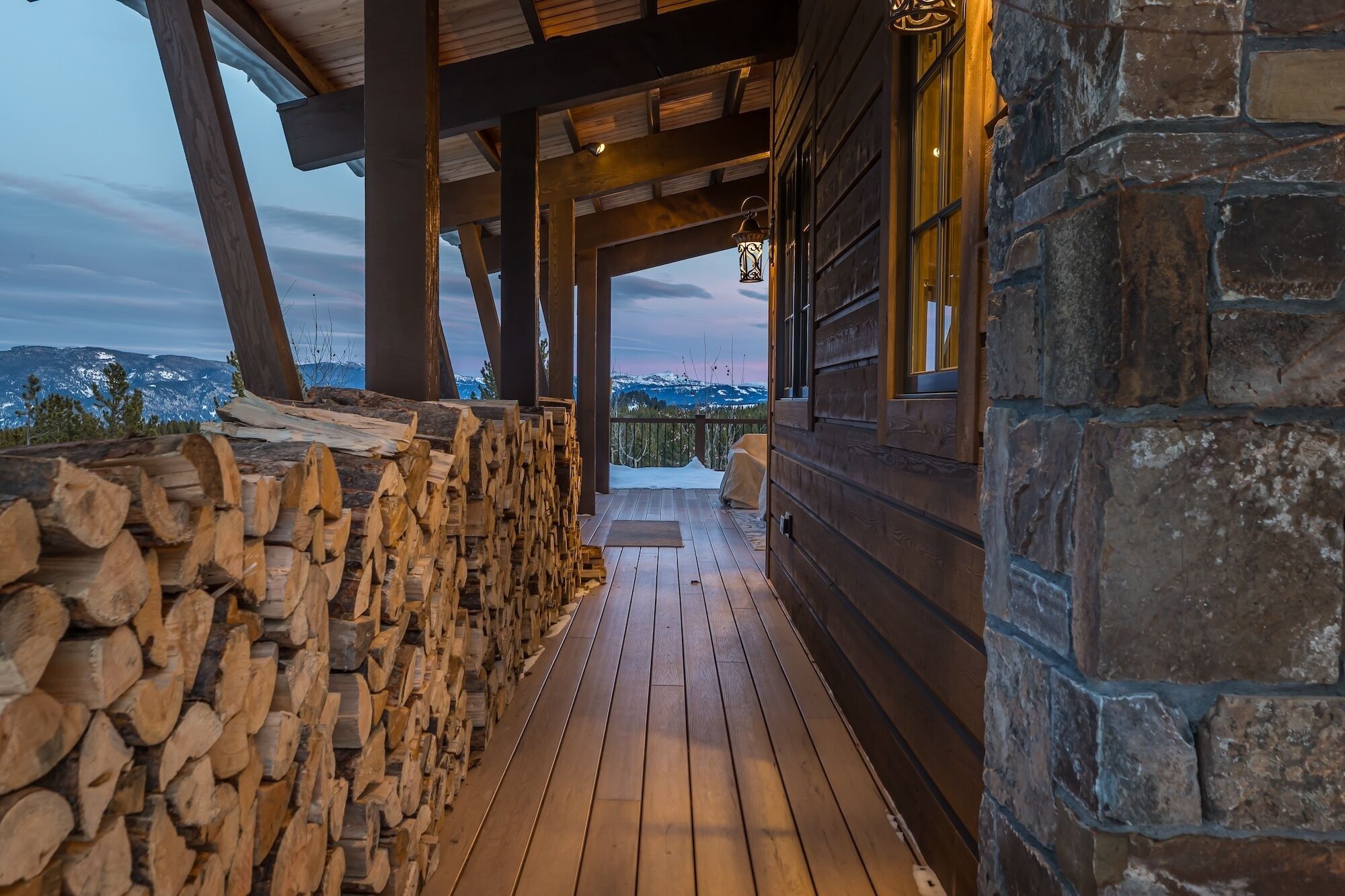 A wooden cabin with a stone exterior, a wooden deck, and a stack of firewood.